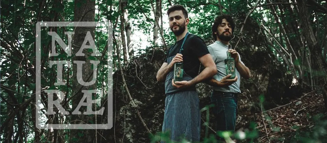 Naturae nasce dalla comune passione di due amici, le botaniche. Scopri questa nuovissima distilleria italiana nata in provincia di Varese. | Topbeer Carlo e Diego della distilleria Naturae, nel bosco con due bottiglie di gin | Topbeer