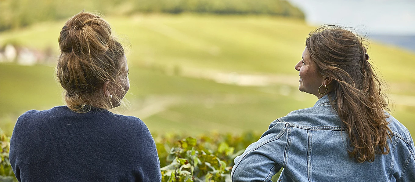 Due donne riprese di spalle mentre parlano in un vigneto